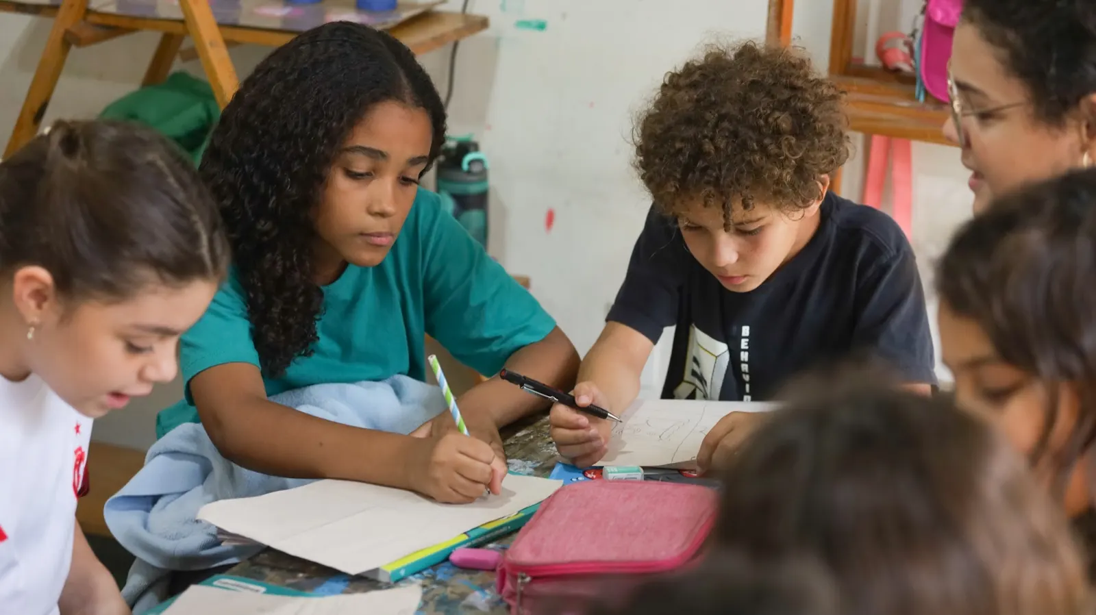 Estudantes escrevem juntos numa mesa coletiva