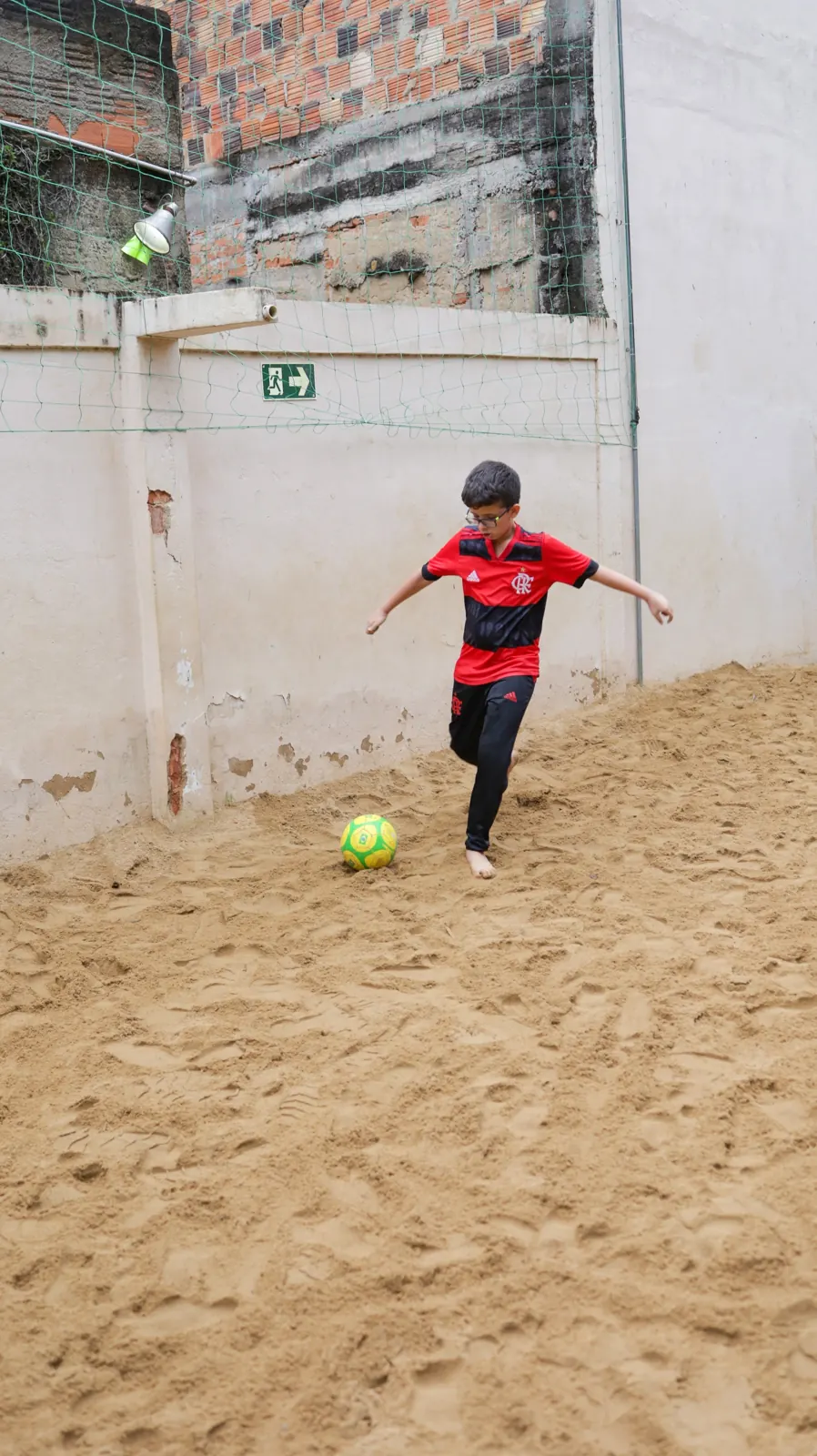 Menino chuta a bola no campinho de areia
